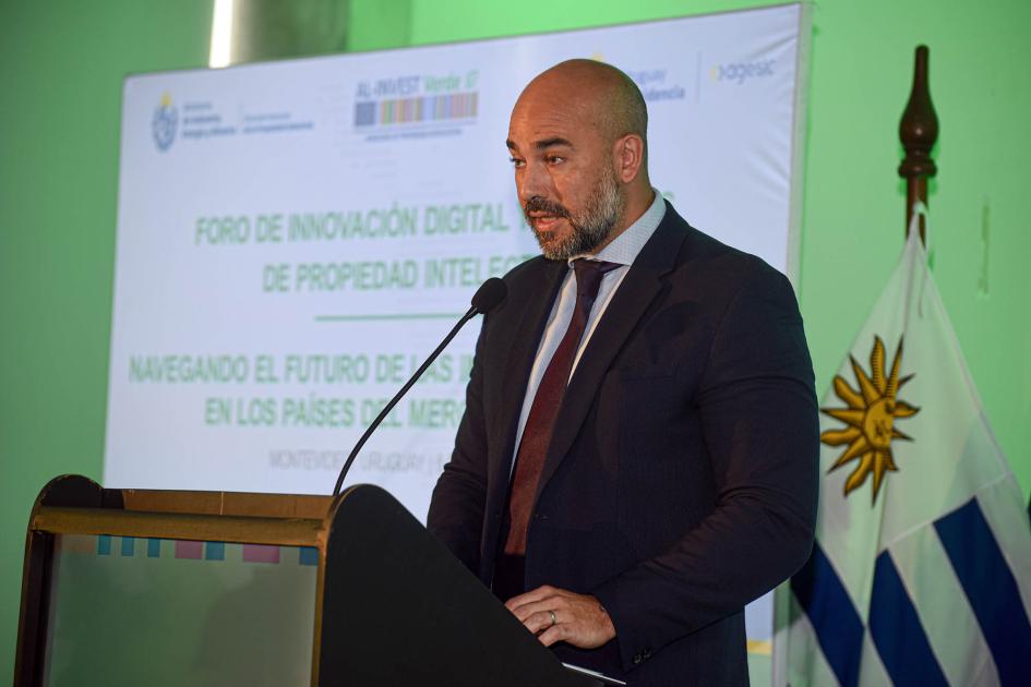 Heber Paguas, director ejecutivo de Agesic Paguas habla desde un atril; detrás, un banner y la bandera uruguaya
