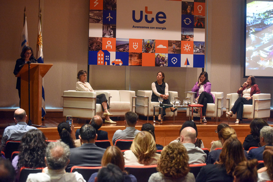 Conversatorio de UTE por el Día Internacional de la Mujer 2026 Al fondo, panel de mujeres sentadas y presidenta Cabrera, de pie; más cerca, público