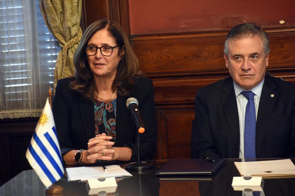 Ministra Facio habla junto al ministro Paganini; en la mesa hay una bandera uruguaya
