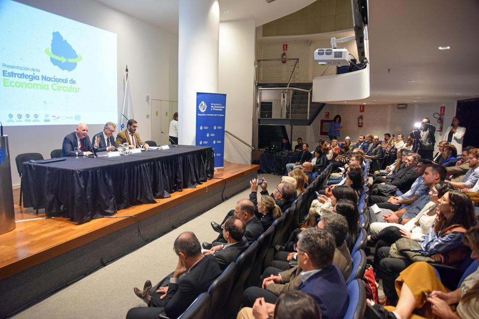 La Estrategia Nacional de Economía Circular fue liderada por cuatro ministerios Al fondo, mesa de autoridades; arriba, una pantalla; a los lados, banners; más cerca, el público