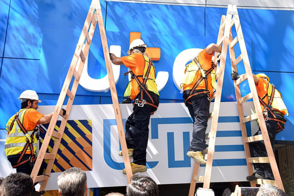 Obreros colocan el nuevo logo de UTE en su stand