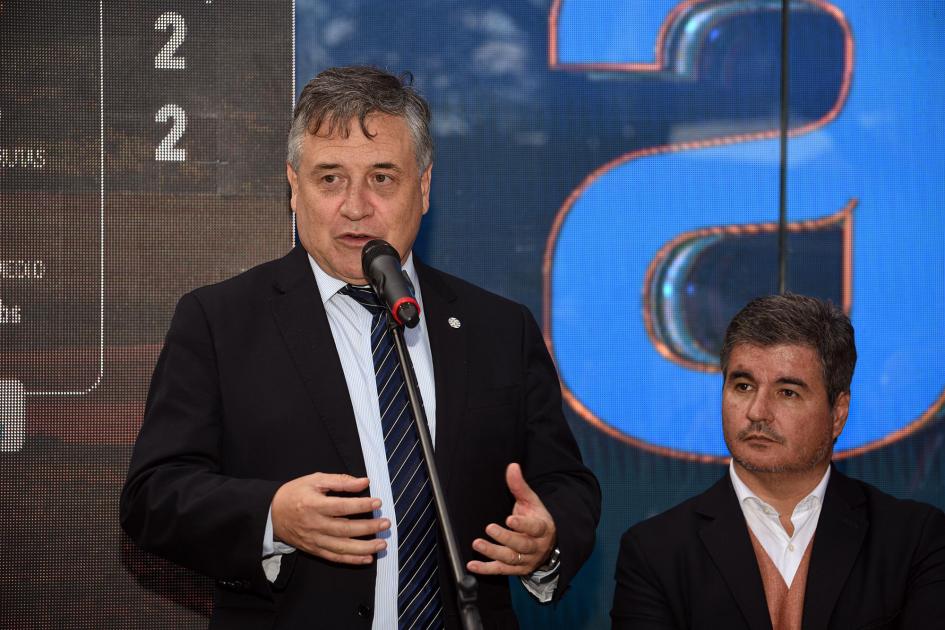 Ministro Omar Paganini en el stand de Antel Paganini habla, junto al director Acosta y Lara, en el stand de Antel; detrás se ve un gran logo
