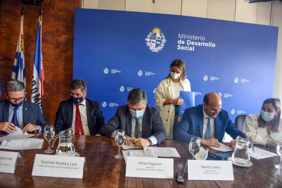 Firma del convenio Autoridades firman el convenio; detrás una mujer les alcanza los documentos