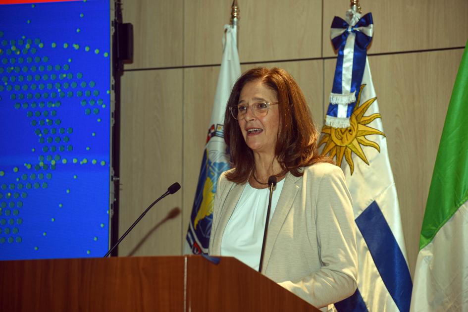 Ministra Facio habla desde un atril; detrás, banderas de Uruguay e Italia, entre otras