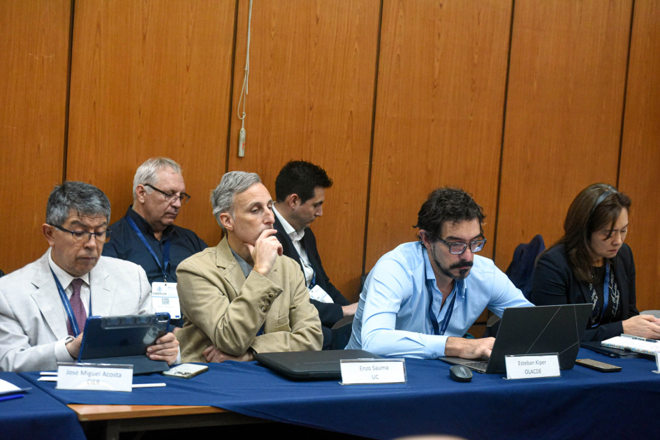 Personas sentadas en una mesa; detrás, segunda fila de personas sentadas