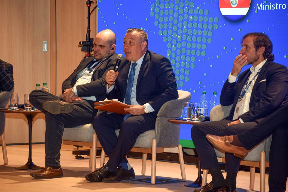 Ministro de Economía, Industria y Comercio de Costa Rica, Francisco Gamboa. Ministro de Costa Rica habla sentado en un sillón; a su lado, oradores
