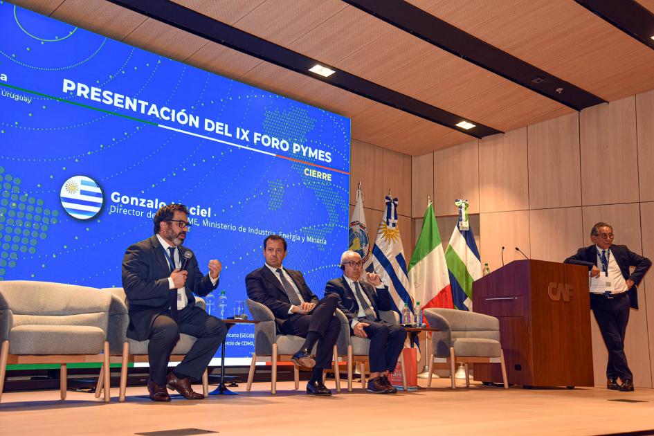 Panel de cierre de la actividad Oradores sentados en sillones; al lado del atril, persona que modera