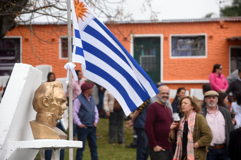 Bandera de Uruguay junto a busto de Artigas. Alrededor gente