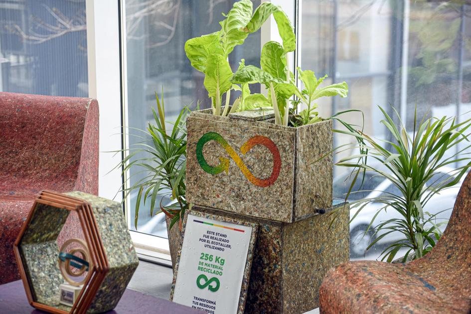 Plantas en macetas de material reciclado, realizadas por un ecotaller, según indica un cartel