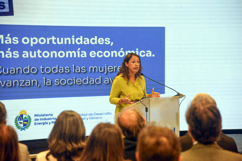 Fernanda Cardona habla a micrófono desde atril. Al fondo pantalla con nombre de la actividad