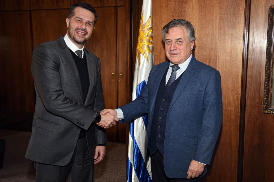 El ministro Paganini lideró el encuentro en que se firmó el acuerdo Paganini da la mano a un hombre; detrás hay una bandera uruguaya