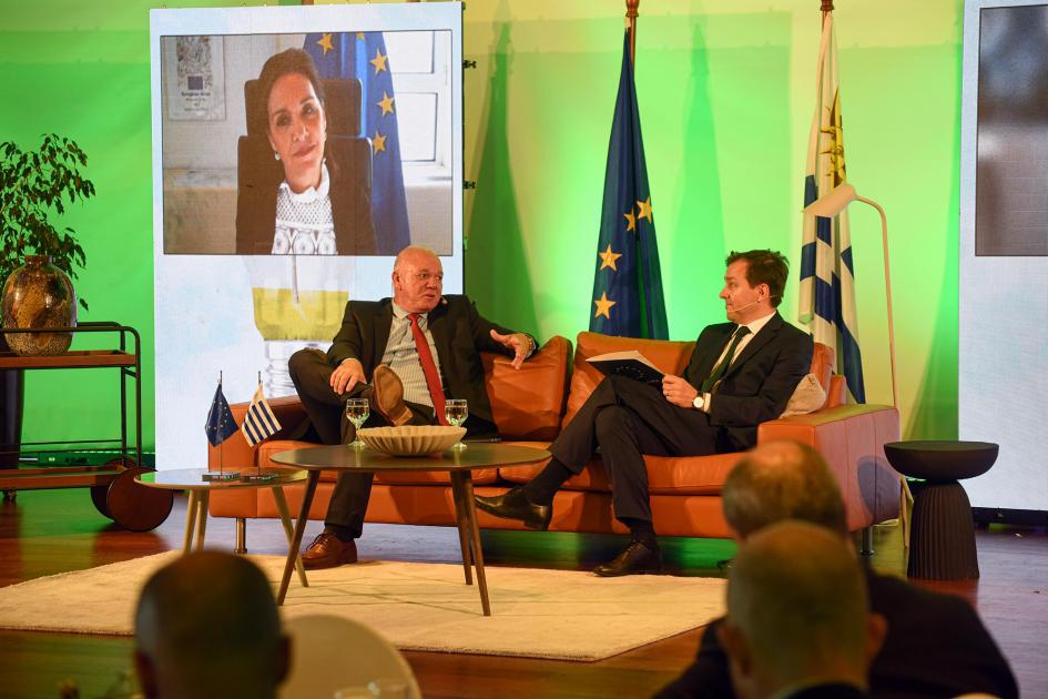 El panel en el que participó Verri se centró en las políticas de estado de transición energética Verri y Kaminski; frente a ellos, participantes; detrás, en una pantalla se ve a una mujer