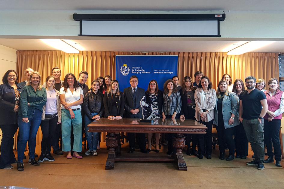 Equipo de trabajo de Dinamige Un gran grupo de hombres y mujeres posan para la foto; frente a ellos hay una mesa pequeña