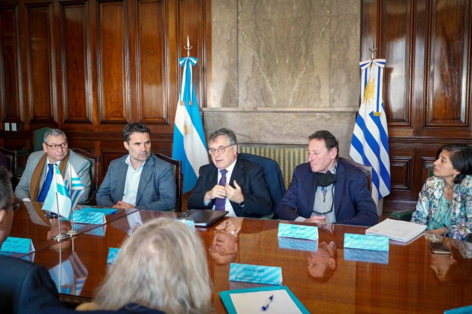 Paganini habla en una mesa al resto de la delegación; detrás, las banderas argentina y urugua