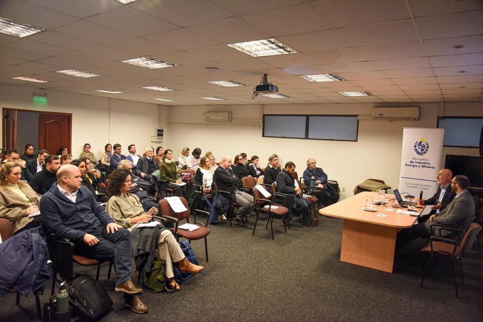 El evento se desarrolló en el salón de actos del MIEM ubicado en Mercedes 1041 Personas reunidas en un salón; a la derecha se ven la mesa de disertantes y un banner del MIEM