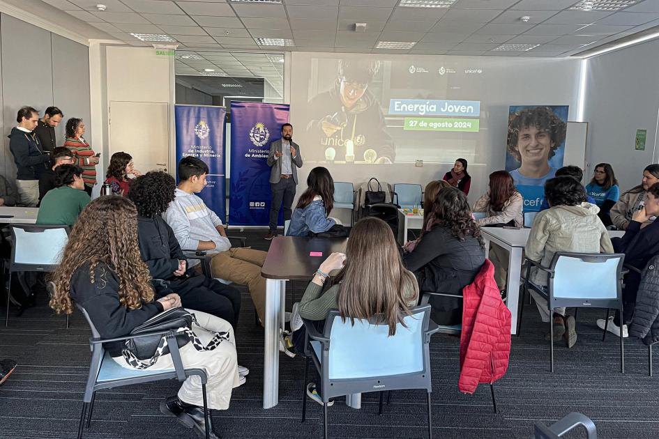 Adolescentes y jóvenes, sentados en mesas; al fondo, de pie, un adulto