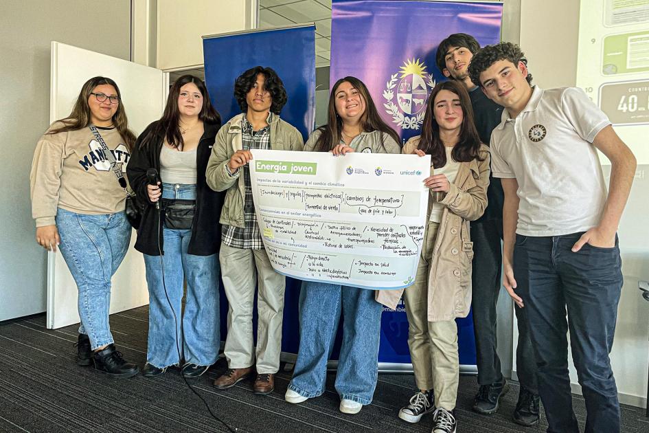 Adolescentes y jóvenes, de pie; algunos sostienen un gran cartel; detrás, banners