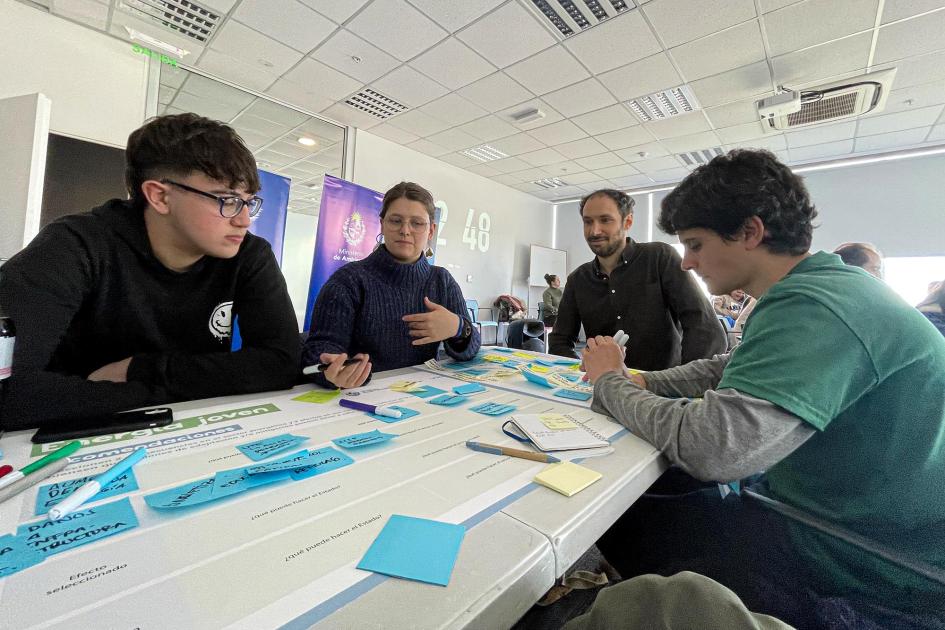 Adolescentes y jóvenes escriben y hablan en una mesa con papeles