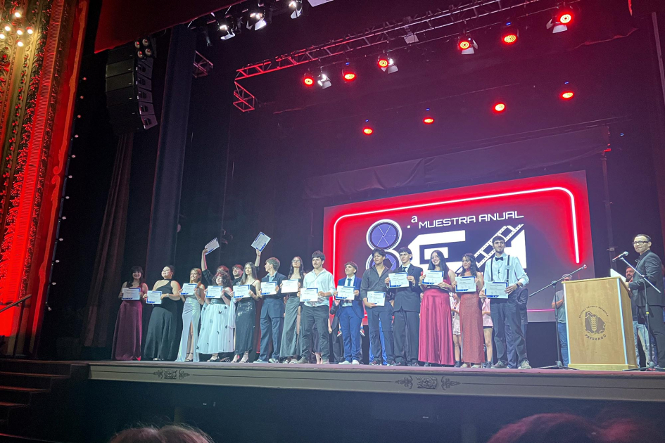 Estudiantes sostienen diplomas sobre el escenario del teatro