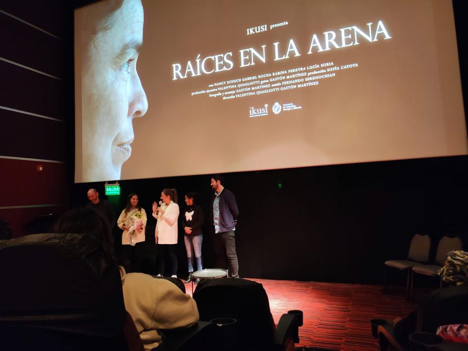 Presentación del corto Protagonistas en un escenario; encima, una pantalla con un fotograma del corto