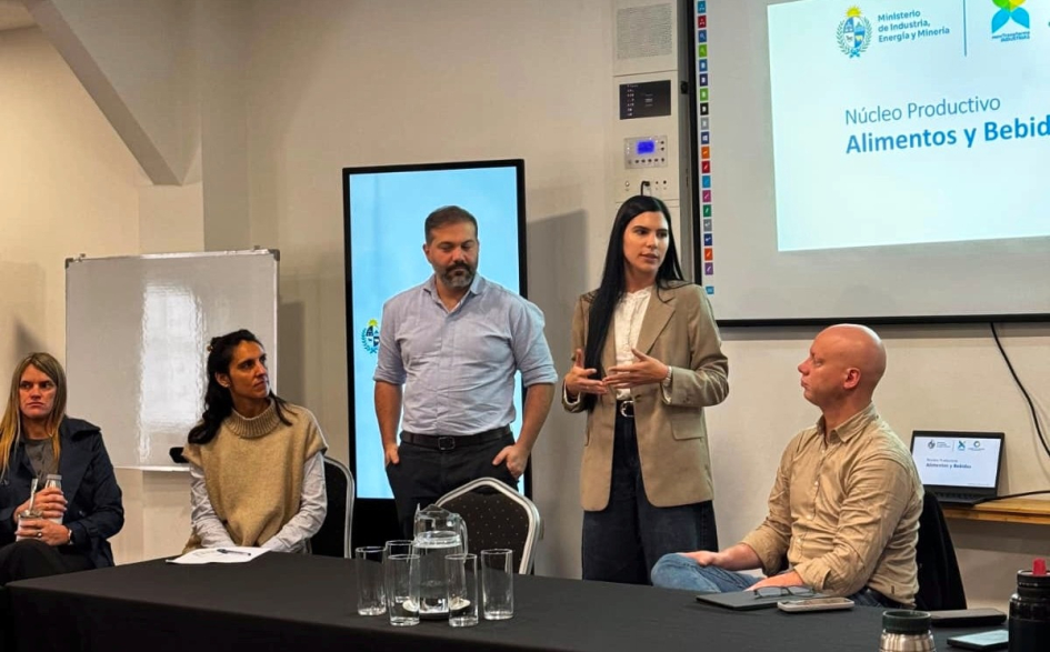 Reunión de trabajo en Maldonado Personas de pie y sentadas en mesa; detrás pantalla y banner institucional