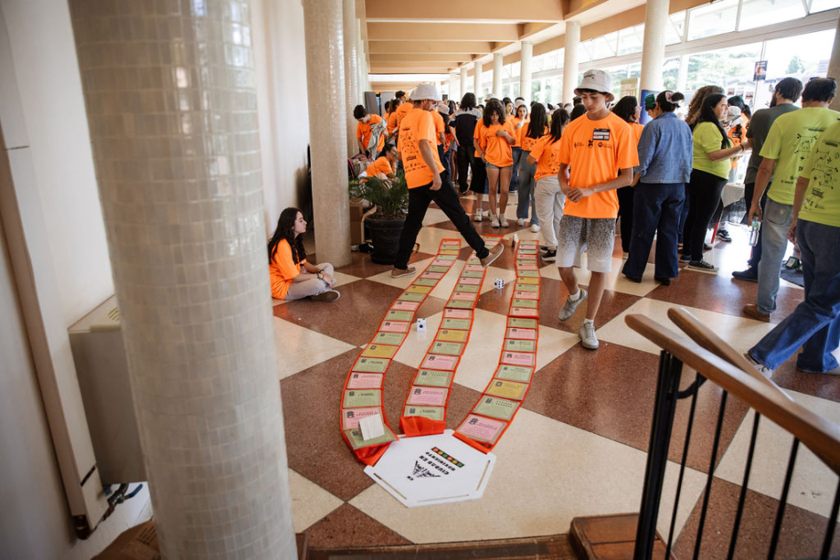 Adolescentes con camisetas naranjas, celestes y verdes. En el piso un juego.