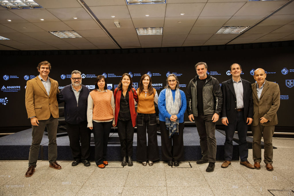 Representantes del comité, de pie, posan para foto; detrás escenario con pantalla