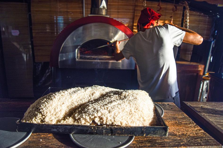 Panadería Masa sobre placa y detrás se ve de un panadero de espalda trabajando con el horno