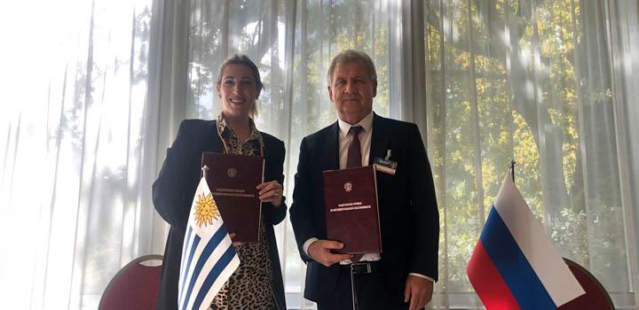 La directora Estrada firmó un memorándum de entendimiento con Rusia Estrada junto al representante de Rusia; se ven banderas de ambos países