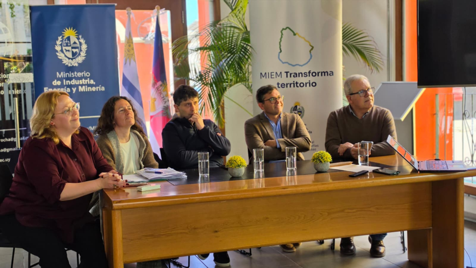 Personas sentadas en una mesa; detrás, banner del MIEM