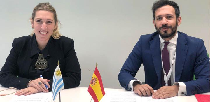 La directora Estrada y el representante de España firmaron un memorándum de entendimiento La directora Estrada junto al representante de España; se ven las banderas de ambos países