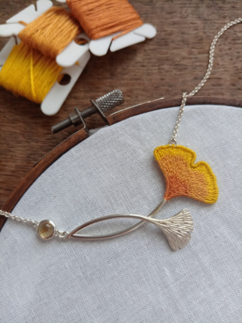 Collar en plateado, con hilos naranja en su diseño y junto a la artesanía