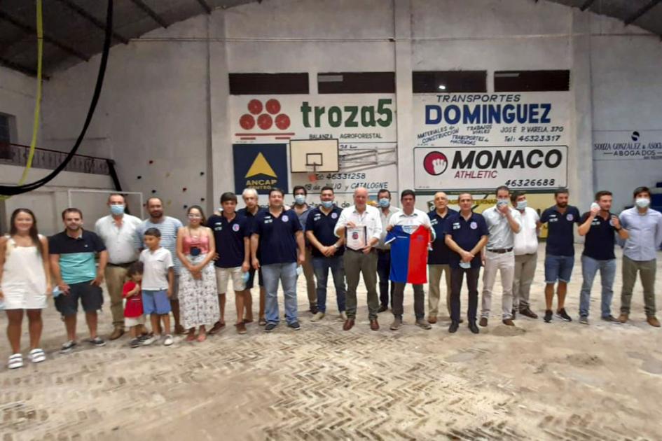 Autoridades, integrantes del Club Estudiantes de Tacuarembó y público Autoridades, miembros del club y otras personas posan en el gimnasio; detrás hay publicidades