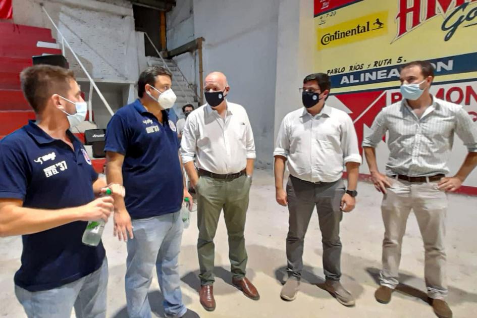 Autoridades e integrantes del Club Estudiantes de Tacuarembó Autoridades e integrantes del club dialogan; detrás hay una pared con publicidades