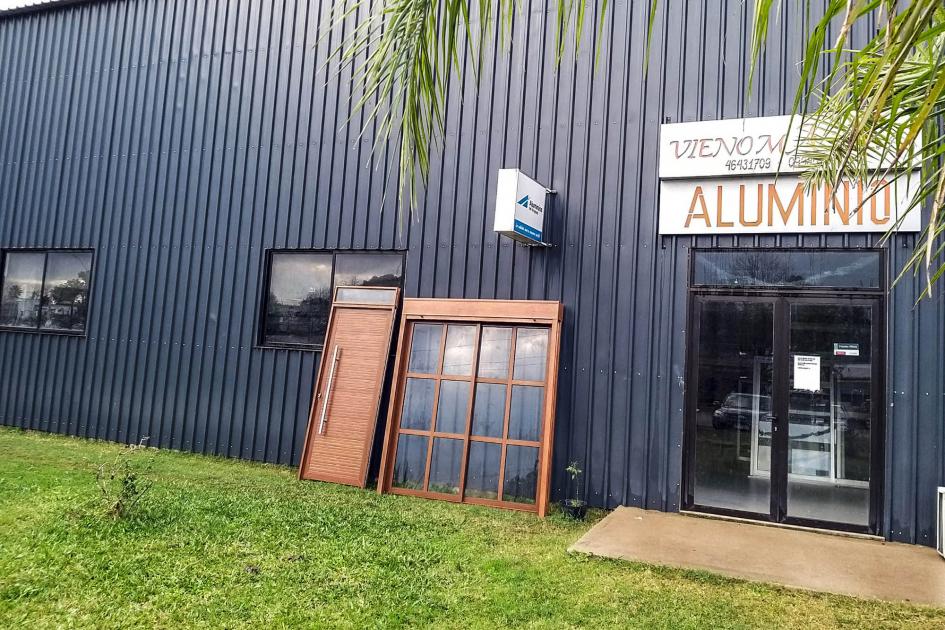 Se ve una ventana en un galpón que afuera dice Vienomas Aluminio