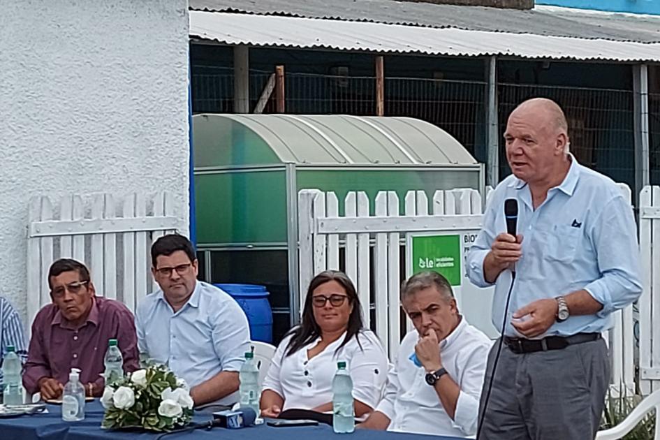 Ministro interino Walter Verri y mesa de autoridades en Villa Sara Verri habla, de pie, junto a la mesa de autoridades