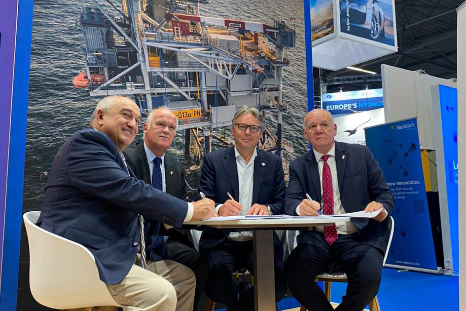 Firma del memorándum de entendimiento entre Uruguay y Países Bajos Cuatro hombres firman un documento (el MOU) en una mesa; detrás hay banners
