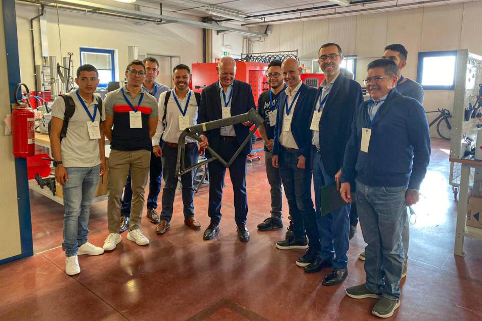 Visita a la fábrica de 3T Bike Verri sonríe sosteniendo un cuadro de bicicleta; está dentro de 3T Bike junto a varios hombres