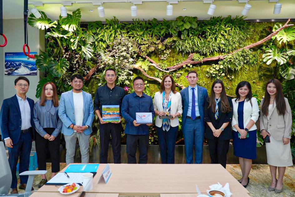 La ministra, junto a un grupo de personas, posan junto a una pared verde, con plantas