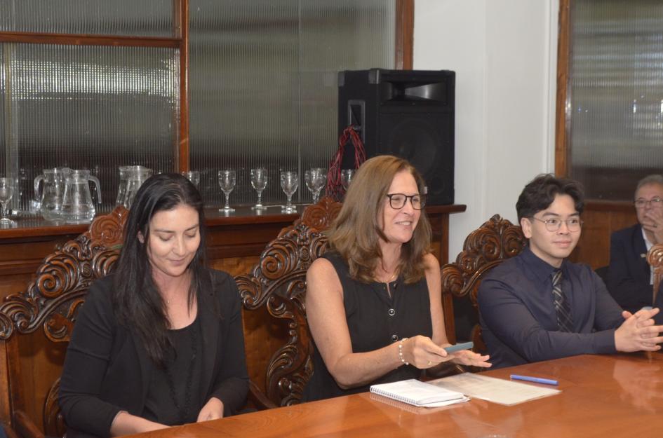 La ministra, sentada en una mesa, junto a un estudiante y una asesora del MIEM