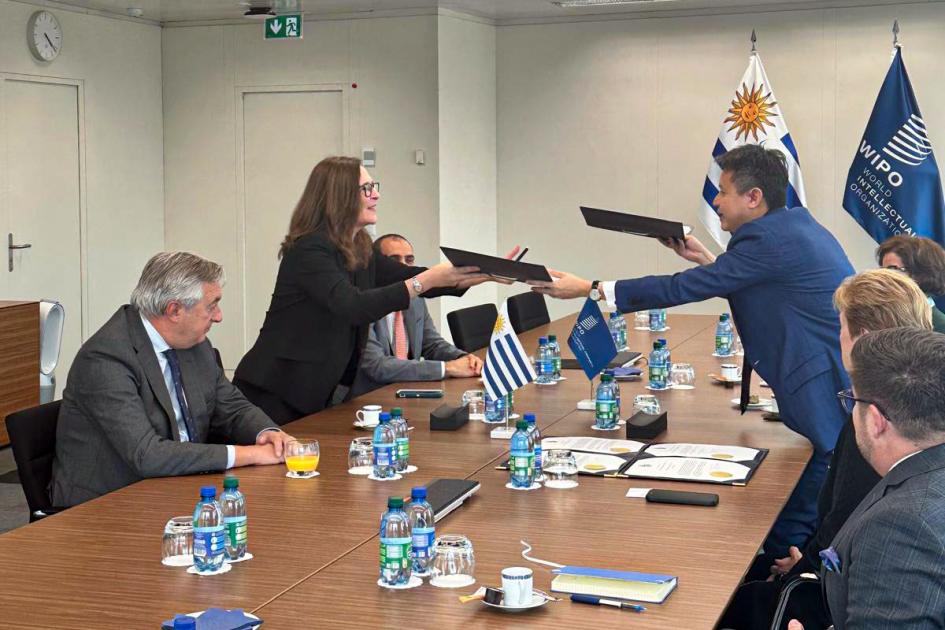 Firma del depósito del instrumento de adhesión de Uruguay al PCT Facio y Tang intercambian carpetas con los documentos, al momento de firmar; a su lado, delegaciones
