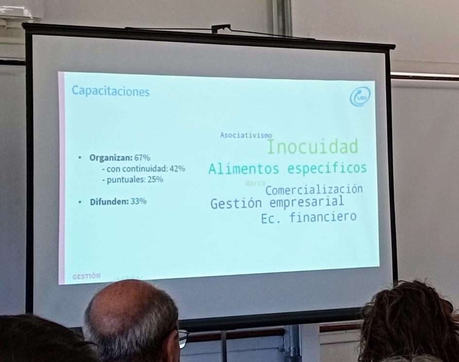 Encuentro nacional de Centros Colectivos de Elaboración de Alimentos Pantalla; la miran personas, cuyas cabezas se ven de espaldas