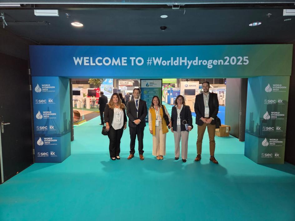 Delegación pública en el evento Ministra y otras personas, en un portal que da la bienvenida (en inglés) al evento