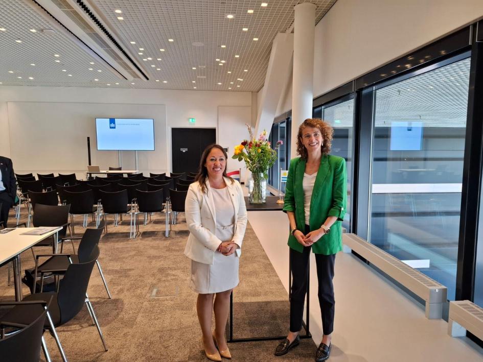 Ministra Fernanda Cardona y ministra Sophie Hermans Ministra Cardona y ministra Hermans, de pie, en una oficina con grandes ventanales