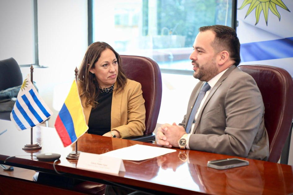 Fernanda Cardona y Edwin Palma Ministra Cardona y ministro Palma sentados. En el escritorio, banderas de Uruguay y de Colombia.