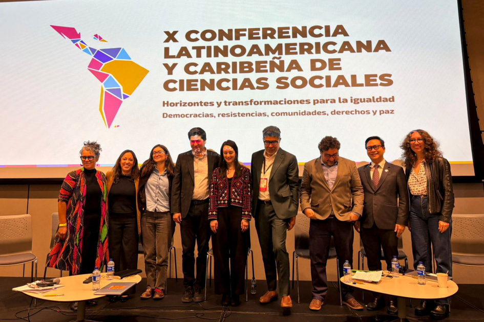 Panel CLACSO 2025 Integrantes del panel parados. Detrás, pantalla con nombre de la conferencia