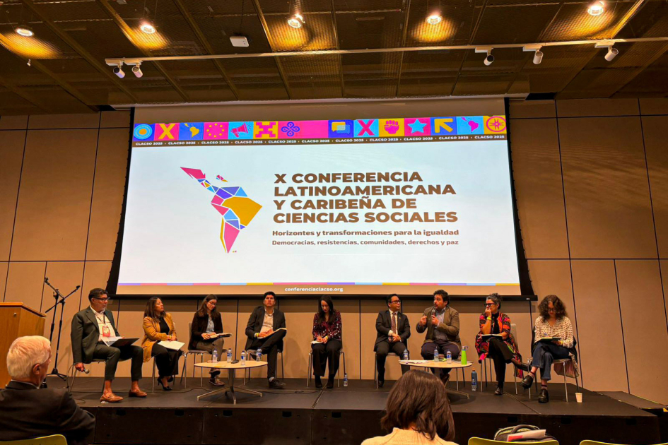 Panel CLACSO 2025 Integrantes del panel sentados. Detrás, pantalla con nombre de la conferencia