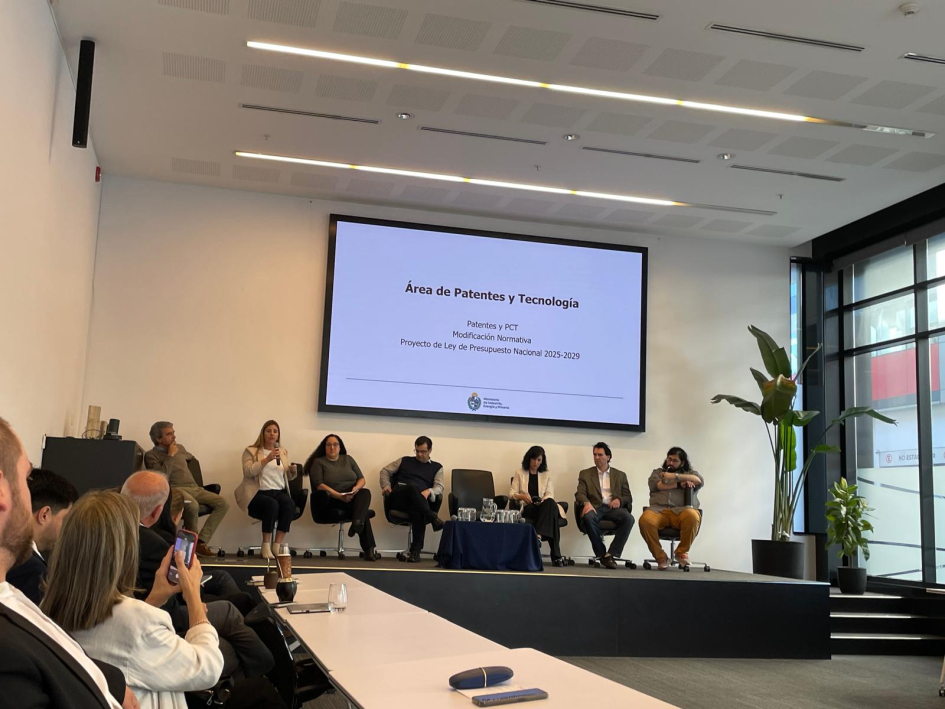 Presentación DNPI Jornadas de la Propiedad Industrial AUDAPI Siete personas sentadas en un escenario y una pantalla detrás