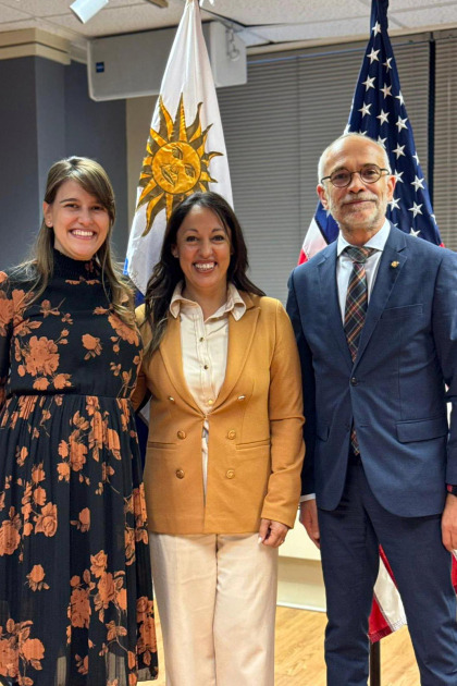 Presentación en la Embajada de Uruguay en Estados Unidos Cardona, embajador Castillos y otra mujer, frente a las banderas de Uruguay y EE. UU.