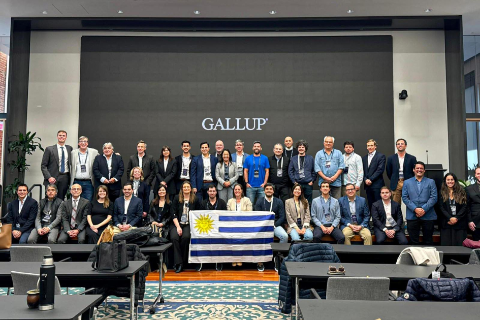 Personas de pie y en cuclillas, con bandera de Uruguay; detrás, banner de Gallup Personas de pie y en cuclillas, con bandera de Uruguay; detrás, banner de Gallup